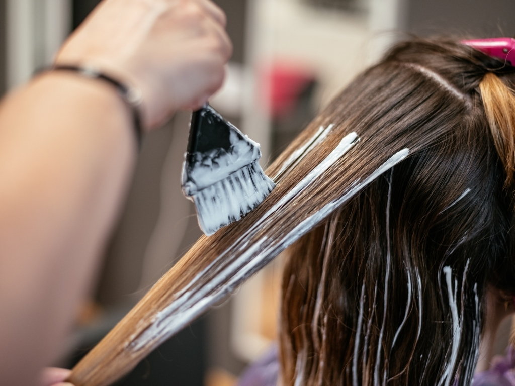 How Do Clip In Hair Extensions Work? A Beginner’s Guide 8 Hair dye being applied with a brush to a section of brown hair