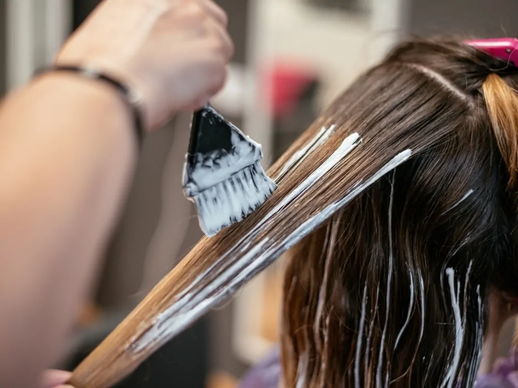 Hair dye being applied with a brush to a section of brown hair