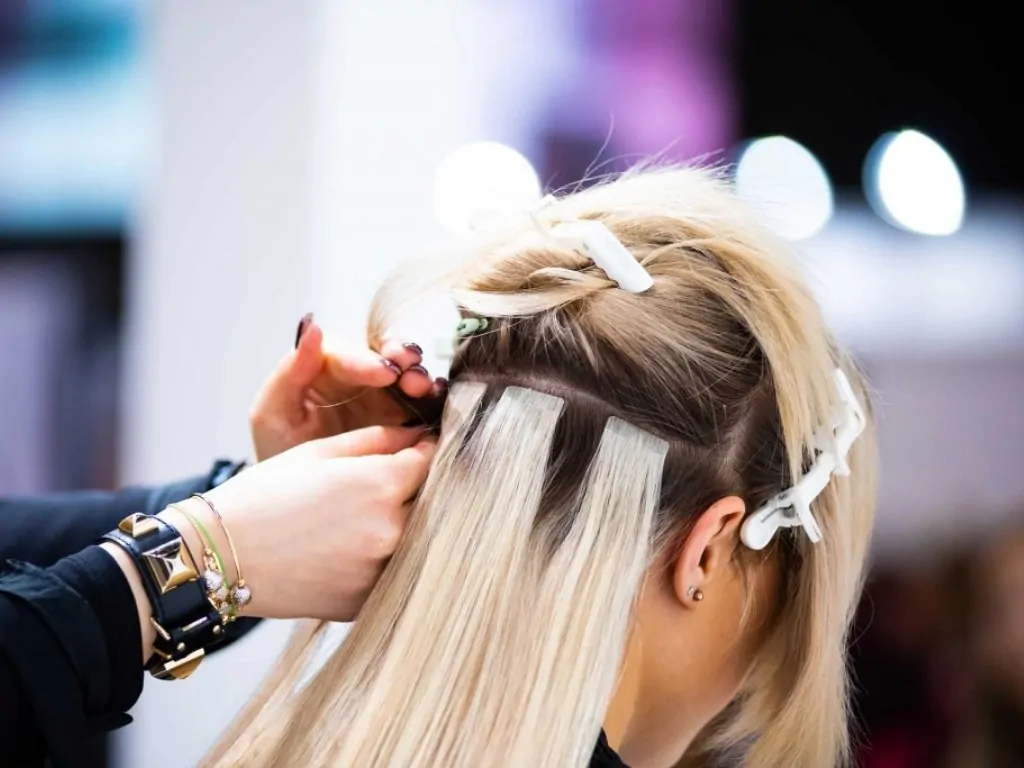 Clip in hair extensions being applied to blonde hair in a salon